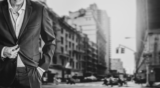 Well dressed businessman standing on busy street in New York. Black and white image with copy space on the blurred background.