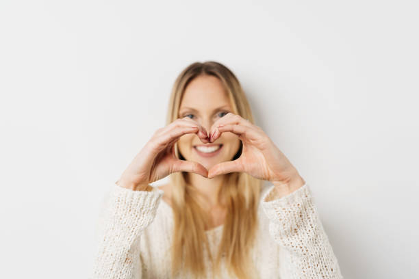 Happy young woman making a romantic heart gesture with her hands in front of her face with focus to her fingers over a white background studio with copy space