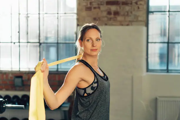 Young woman working out with gym bands or ribbons to stretch and tone her muscles standing in an urban gymnasium with copy space