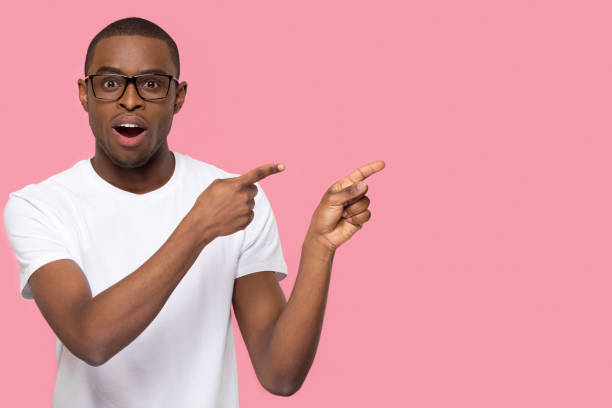 Surprised black man pointing fingers at copyspace looking at camera