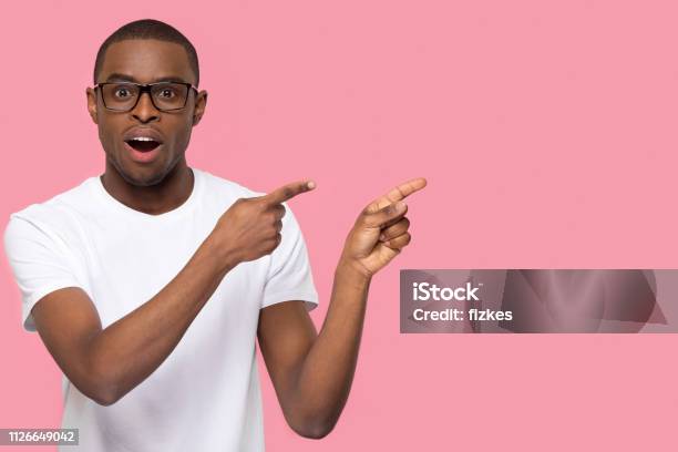 Surprised Black Man Pointing Fingers At Copyspace Looking At Camera Stock Photo - Download Image Now