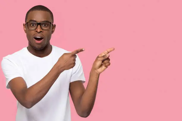 Photo of Surprised black man pointing fingers at copyspace looking at camera