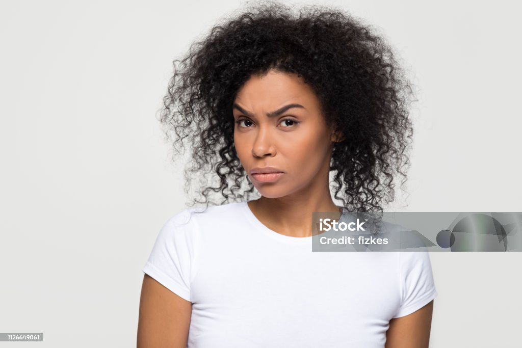 Suspicious african woman with distrustful face looking at camera Suspicious annoyed young african american woman with distrustful face looking at camera, skeptical sarcastic black girl feeling cautious dubious distrusting isolated on grey white studio background Women Stock Photo