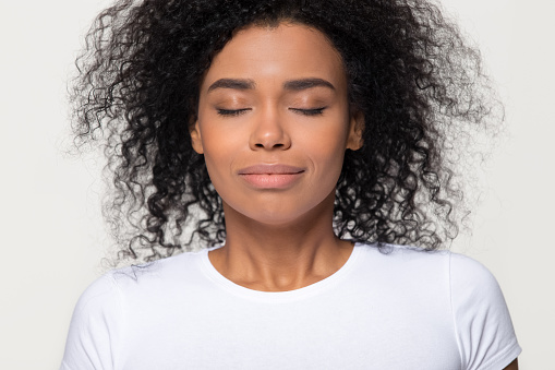 Happy calm african woman with beautiful face take deep breath of fresh air, grateful mindful black lady enjoy inhaling meditating feel no stress free harmony isolated on white grey studio background