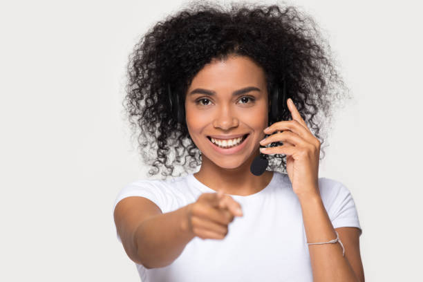 улыбаясь африканская женщина носить гарнитуру глядя указывая пальцем на камеру - administrator telephone office support стоковые фото и изображения