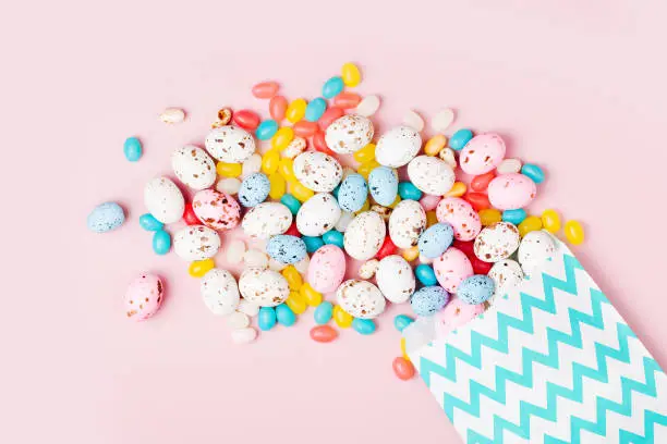 Easter candy chocolate eggs and Jellybean flowing from party paper bag  on pink background