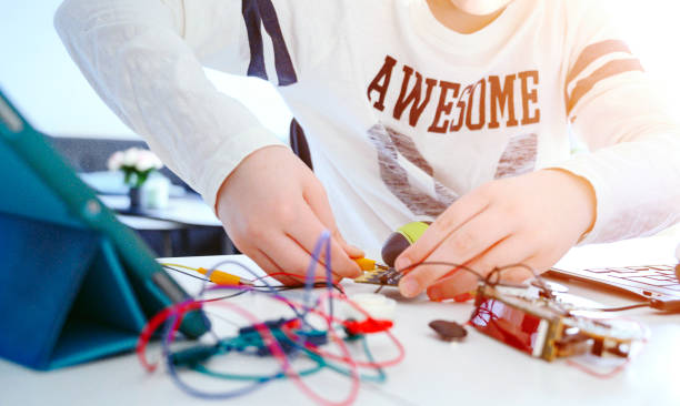 Close up of a boy working with electronics. He sits a table and has a laptop computer that makes him able to code and make programs.