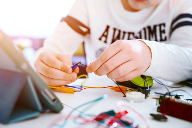 Close up of a boy working with electronics. He sits a table and has a laptop computer that makes him able to code and make programs.