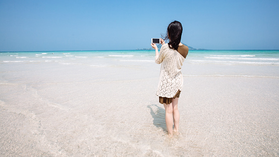 A Female Traveler Takes Picture of the Turquoise Ocean with a Cellphone Camera (Jeju Island) horizontal