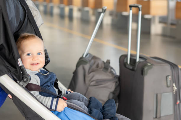 cute funny caucasian baby boy sitting in stroller near luggage at airport terminal. child sin carriage with suitcasese near check-in desk counter. travelling with small children concept - airport airport check in counter arrival departure board checkout counter imagens e fotografias de stock