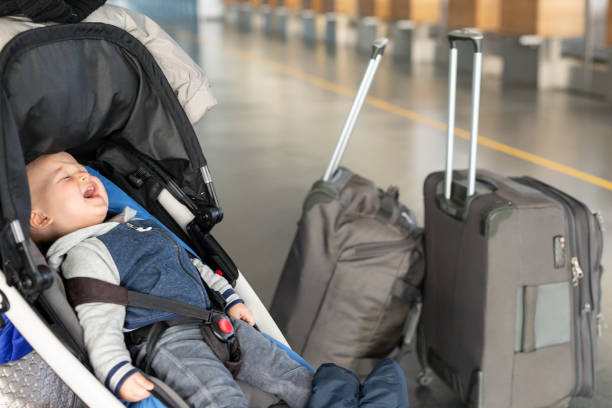 screaming baby boy sitting in stroller near luggage at airport terminal. child in carriage near check-in desk counter. children tears , panic and hysterics. travelling with small children concept - airport arrival departure board airport check in counter airplane imagens e fotografias de stock