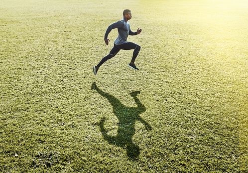Full length shot of a handsome and athletic young man running across an open field