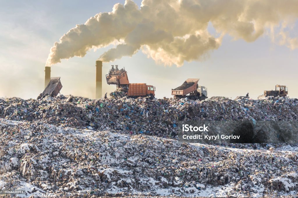 Dump trucks unloading garbage over vast landfill. Smoking industrial stacks on background. Environmental pollution. Outdated method of waste disposal. Survival of times past Dump trucks unloading garbage over vast landfill. Smoking industrial stacks on background. Environmental pollution. Outdated method of waste disposal. Survival of times past. Landfill Stock Photo