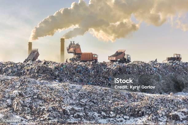 Dump Trucks Unloading Garbage Over Vast Landfill Smoking Industrial Stacks On Background Environmental Pollution Outdated Method Of Waste Disposal Survival Of Times Past Stock Photo - Download Image Now