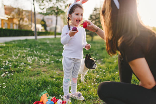 I love the easter egg hunt! Cute little four year old girl enjoying  Easter egg hunt in a public park with her family breed eggs stock pictures, royalty-free photos & images