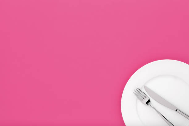 istock Fork and knife on white round ceramic plate on light purple background with copy space. Top down view. 1126669099