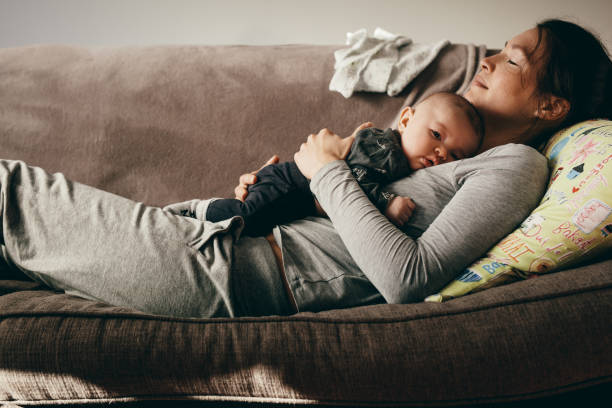 mother sleeping on a couch with her baby on her - baby mother sleeping child imagens e fotografias de stock