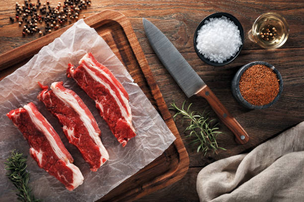 costola corta in vitello crudo su carta da cucina bianca e tavolo da taglio in legno. - braciola foto e immagini stock