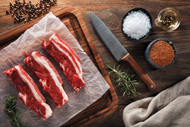 Raw calf short rib on white cooking paper and wooden cutting table. Raw calf short rib on white cooking paper and wooden cutting board. Decorated with herbs, spices and chef's knife. Overhead view. rib cage stock pictures, royalty-free photos & images