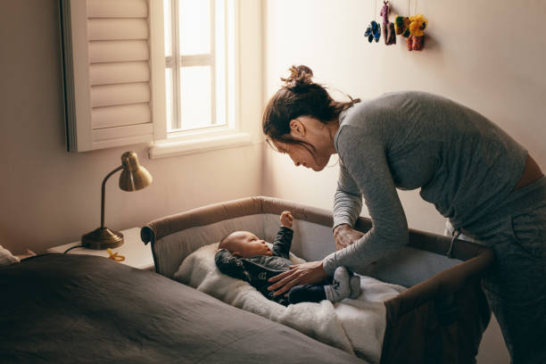 joven madre mirando a su bebé dormir en una cuna - baby mother sleeping child fotografías e imágenes de stock