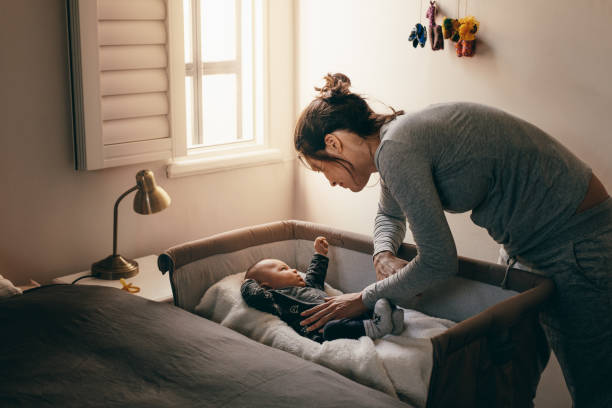 Young mother looking at her baby sleeping in a crib Mother putting her baby to sleep on a bedside baby crib. Woman bending forward over a crib to check her sleeping baby. crib photos stock pictures, royalty-free photos & images