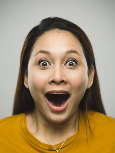 Real malaysian young woman with surprised expression Close up portrait of asian young woman with surprised expression against white gray background. Vertical shot of malaysian real people laughing and surprised in studio with long brown hair. Photography from a DSLR camera. Sharp focus on eyes. asian woman mouth open stock pictures, royalty-free photos & images