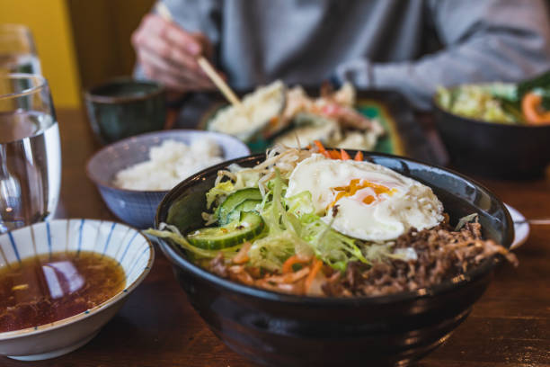 Korean Bibimbap dish Organic korean Bi bim bap dish with rice, cucumber, beef,kochujang sauce, bean sprouts and carrots in a healthy meal on a table with other asian food served in the background. rice bowl restaurant stock pictures, royalty-free photos & images