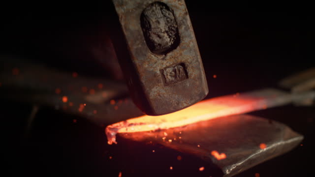 SUPER SLOW MOTION: Metalworker forging a hot piece of metal into a knife blade.