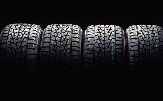 close up on a pile of four new car tires on black background