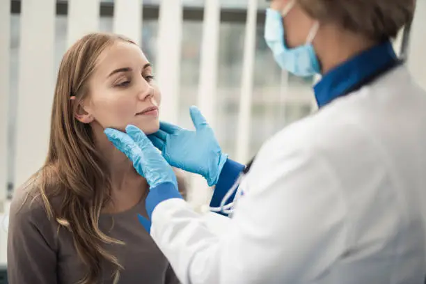 Concept of professional consultation in therapist system. Close up portrait of doctor woman examining tonsils of smiling young lady in medical office
