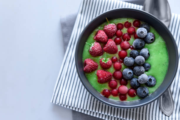 istock Breakfast kiwi smoothie bowl topped with frozen raspberry, blueberry and red currant on gray wooden background. Top view. Copy space 1126698979
