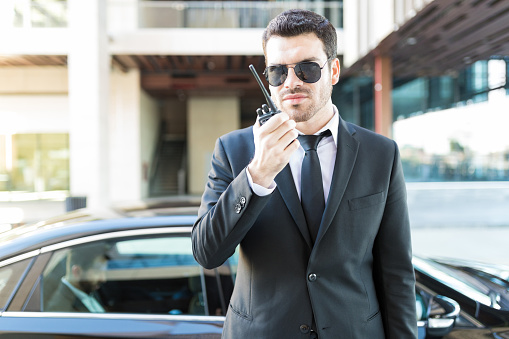 Elegant secret service agent using walkie-talkie to avoid danger for wealthy businessman in car