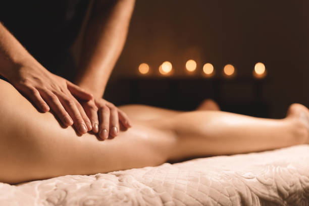 массажист в темной комнате делает массаж тазобедренного сустава маслом для женщины. спа-процедуры массаж женщины - masseur стоковые фото и изображения