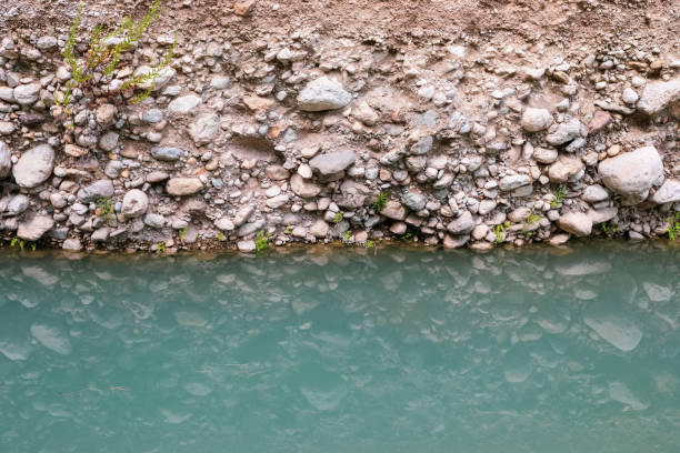 Stone shore of river and its reflection in turquoise calm smooth water surface.