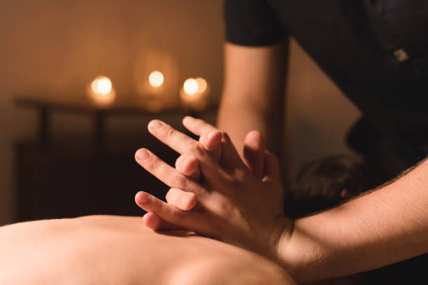 mains d’hommes faire un cou thérapeutique de massage pour une fille couché sur un divan de massage dans un spa de massage avec éclairage sombre. gros plan. touche noire - massaging massage therapist rear view human hand photos et images de collection