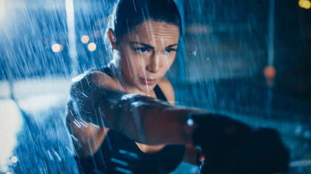 Beautiful Sporty Fitness Girl is Doing Sharowboxing Exercises. She is Doing a Workout at Night in Heavy Rain with One Light Behind Her. Beautiful Sporty Fitness Girl is Doing Sharowboxing Exercises. She is Doing a Workout at Night in Heavy Rain with One Light Behind Her. fist human hand punching power stock pictures, royalty-free photos & images