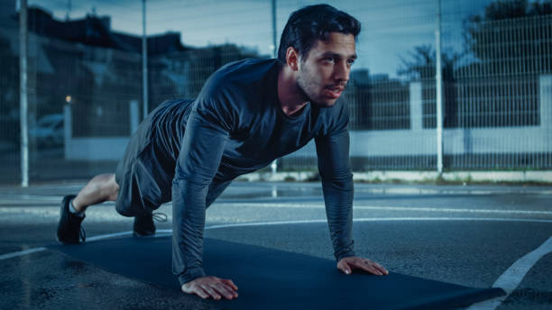 istock Strong Muscular Fit Young Man in Sport Outfit Doing Push Up Exercises. He is Doing a Workout in a Fenced Outdoor Basketball Court. Evening Shot After Rain in a Residential Neighborhood Area. 1126704085