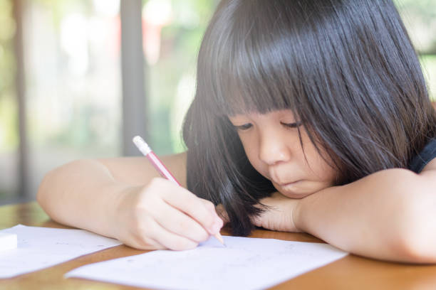 Asia kid girl doing boring homework with bored feeling at home. Female cute child concentrate write on paper. Asian students practice math subject for test. Student study at house Asia kid girl doing boring homework with bored feeling at home. Female cute child concentrate write on paper. Asian students practice math subject for test. Student study at house math homework stock pictures, royalty-free photos & images