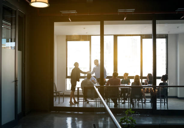 Defocussed image of Business people during a meeting with high rise buildings in the background. They are sitting in a board room, All are casually dressed.