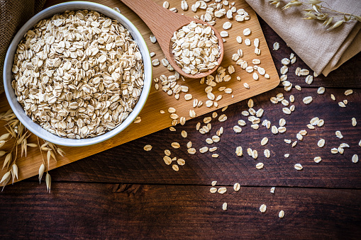 Top view of a bowl filled with uncooked oat flakes with a wooden spoon on wooden table. There is a useful copy space in the lower right corner