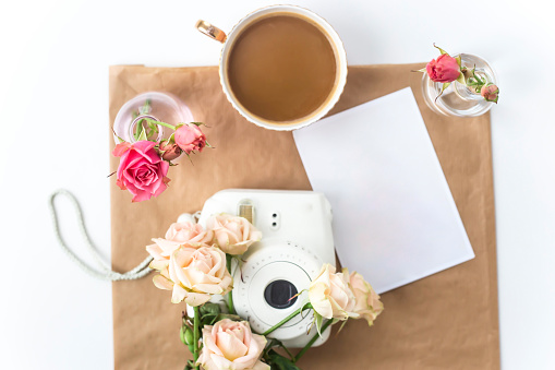 White camera on the desktop among the flowers next to a cup of coffee. Top view, flat lay