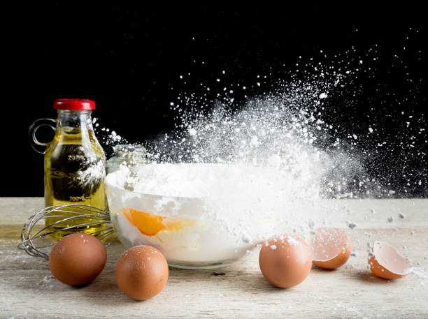 istock Baking Ingredients (eggs,flour,olive oil) on table wood,Flying flour 1126719925