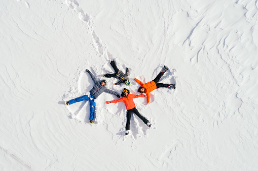 Portrait of cheerful happy family enjoying and having fun while lying down on snow and making snow angels