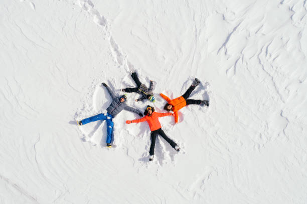 Happy family lying on back on snow Portrait of cheerful happy family enjoying and having fun while lying down on snow and making snow angels snow angels stock pictures, royalty-free photos & images