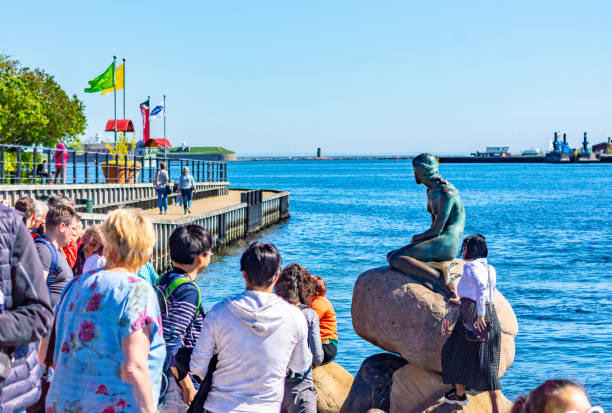 The Little Mermaid Statue by sculptor Edvard Eriksen, which was unveiled on 23 August 1913. A mermaid is a legendary aquatic creature with the upper body of a female human and the tail of a fish, character of fairy tale of Hans Christian Andersen. Today is iconic symbol of Copenhagen, Denmark. surrounded by tourists.