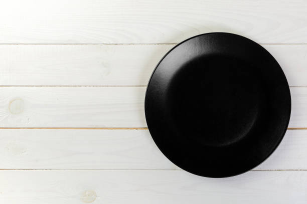 istock Directy above Empty black matte plate on white wooden background with copy space 1126727617