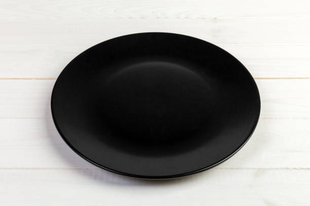 istock Perspective view. Empty black matte plate on white wooden background 1126727625