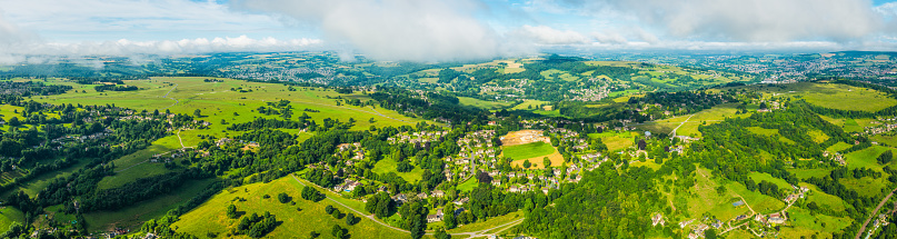 Summer skies and white fluffy clouds above country villages, rolling hills, green fields and the picturesque patchwork pasture of this rural panorama from high above.