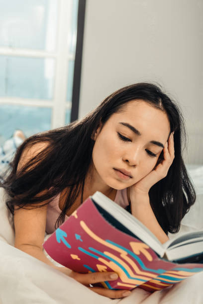 istock Young dark-haired woman reading book while lying in bed 1126729479