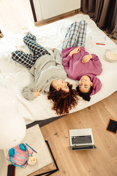 istock Two girlfriends wearing squared pajama trousers lying in bedroom 1126729529